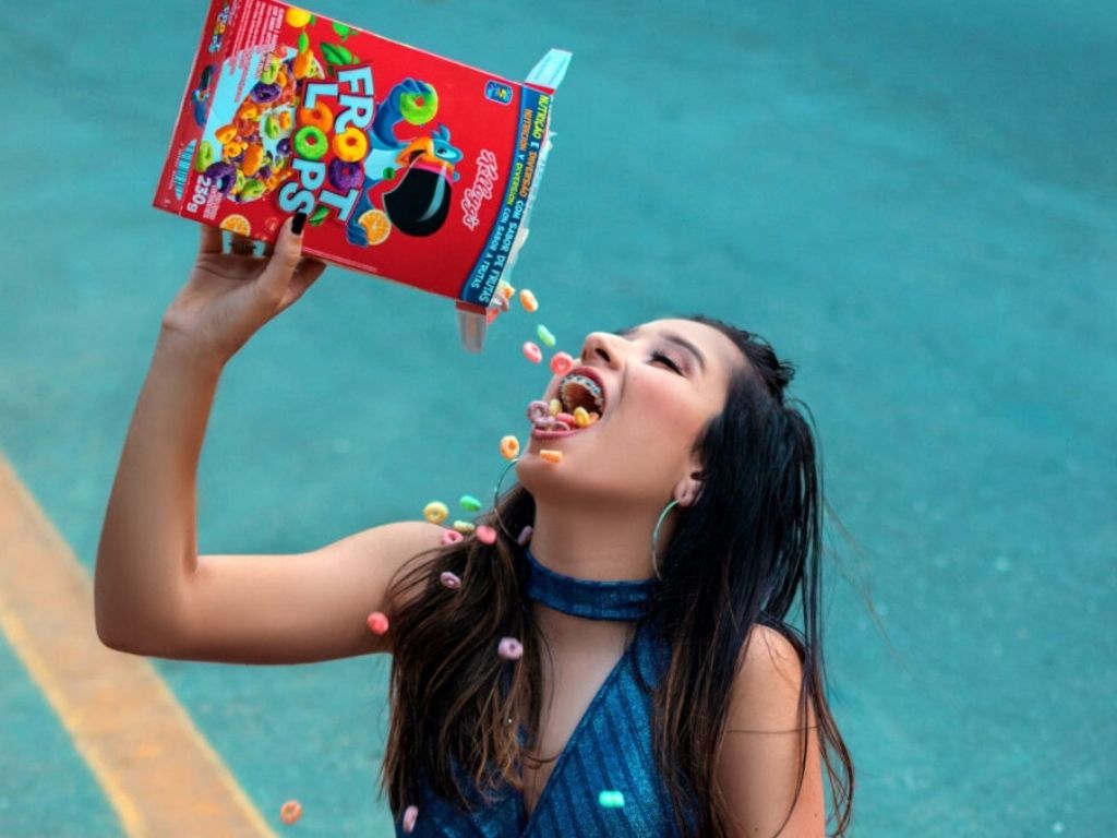 Woman sitting by pool pouring box of fruit loop cereal in her mouth