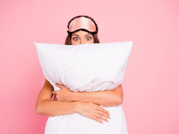 Young shocked woman wearing eye mask, hugging a pillow