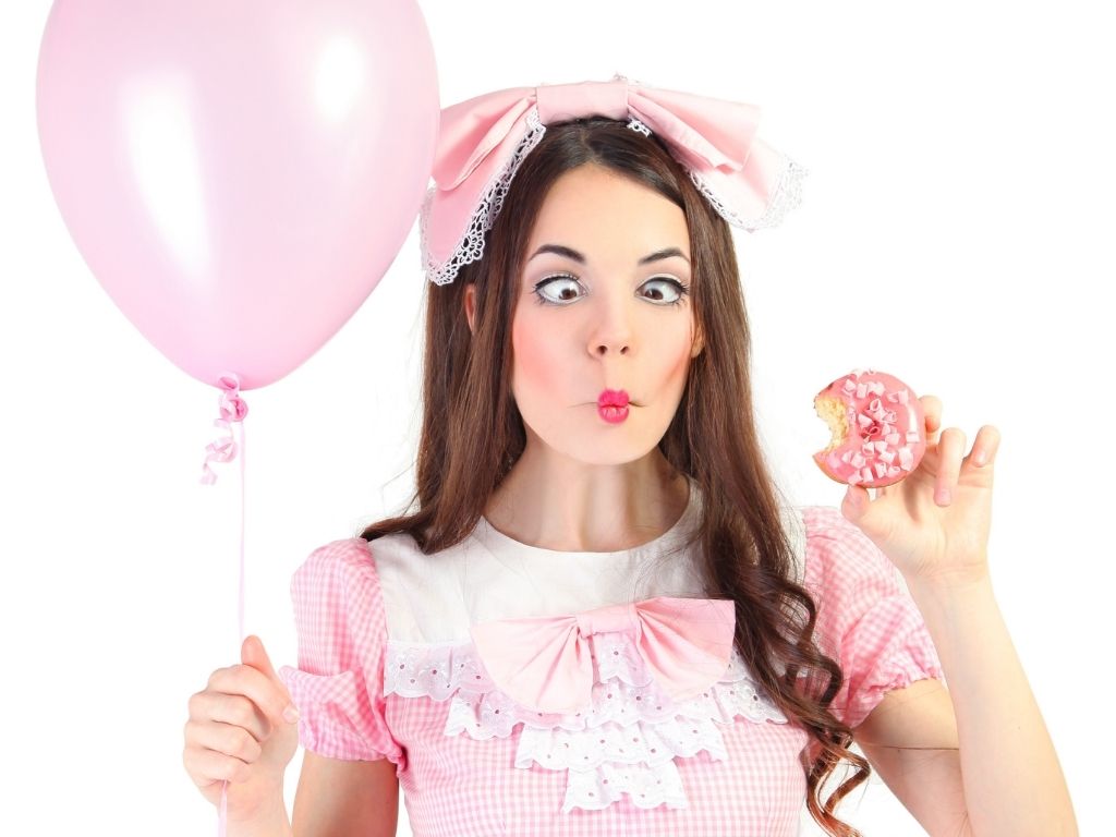Girl making fish face wearing pink dress, pink bow, and holding pink donut
