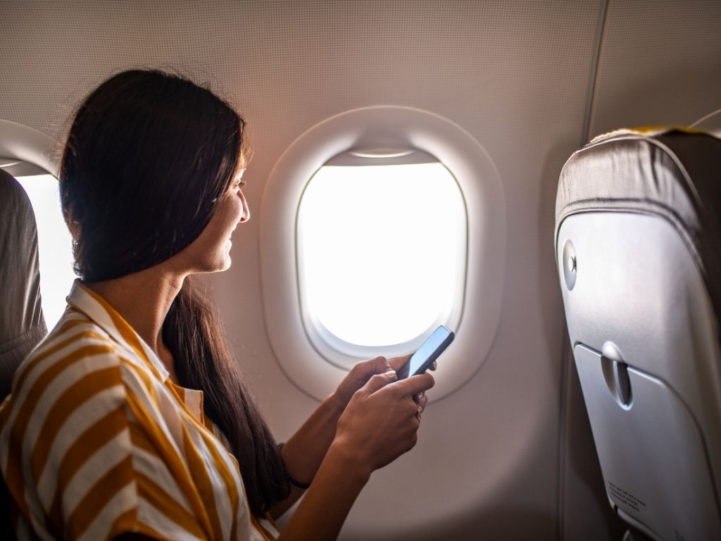 Young smiling Latin Woman using mobile phone on airplane