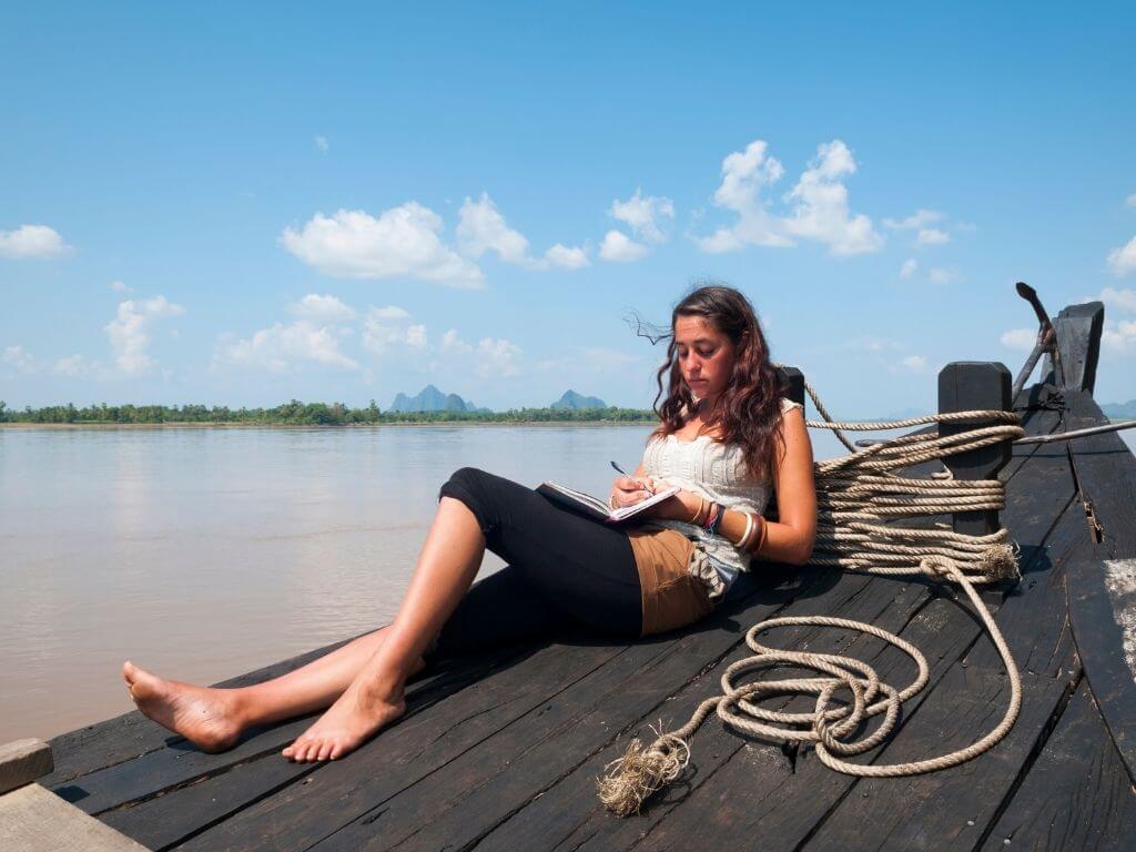 Woman laying on dock by water writing in journal