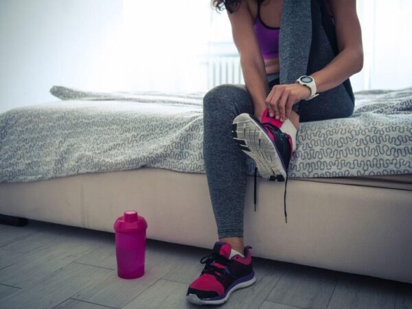 Woman sitting on bed putting on running shoes