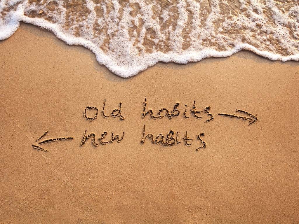 old habits vs new habits concept written in sand on beach