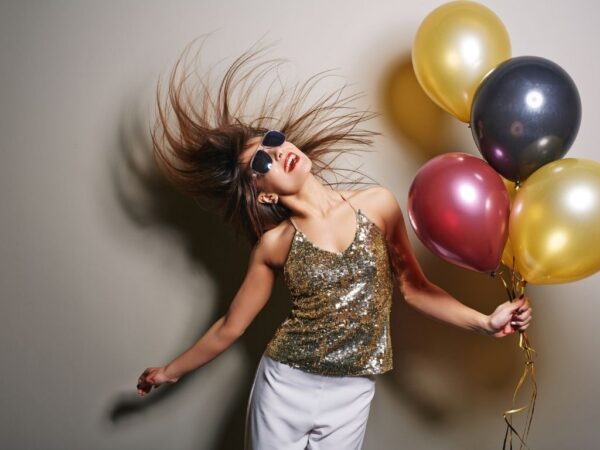 Woman in gold sequin top flipping her hair holding balloons