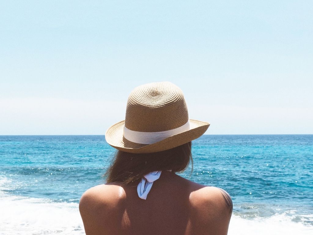 Woman in hat sitting on beach watching ocean