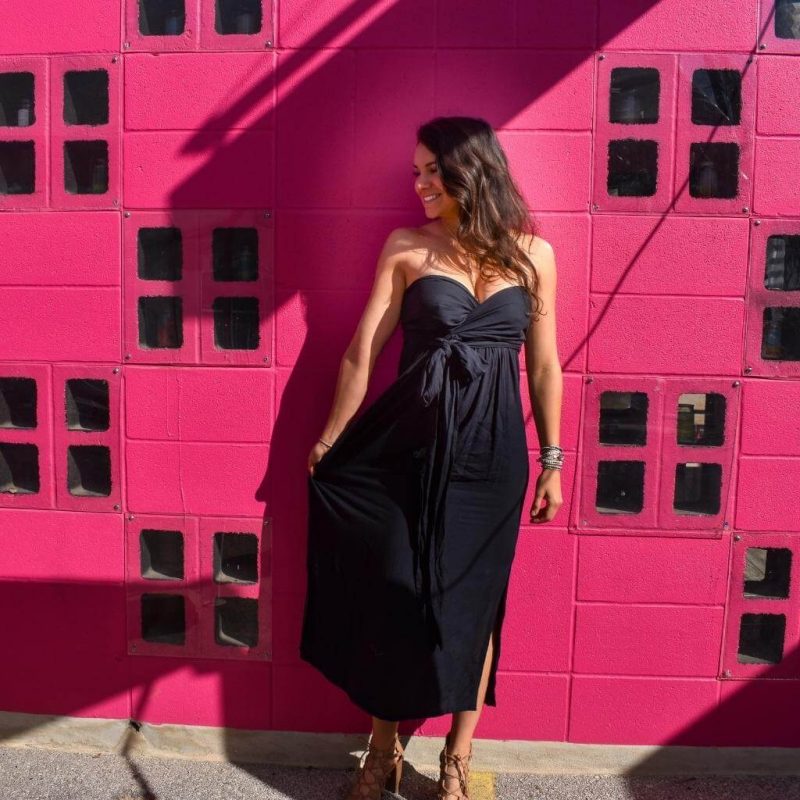 Brunette in black dress leaning on hot pink wall